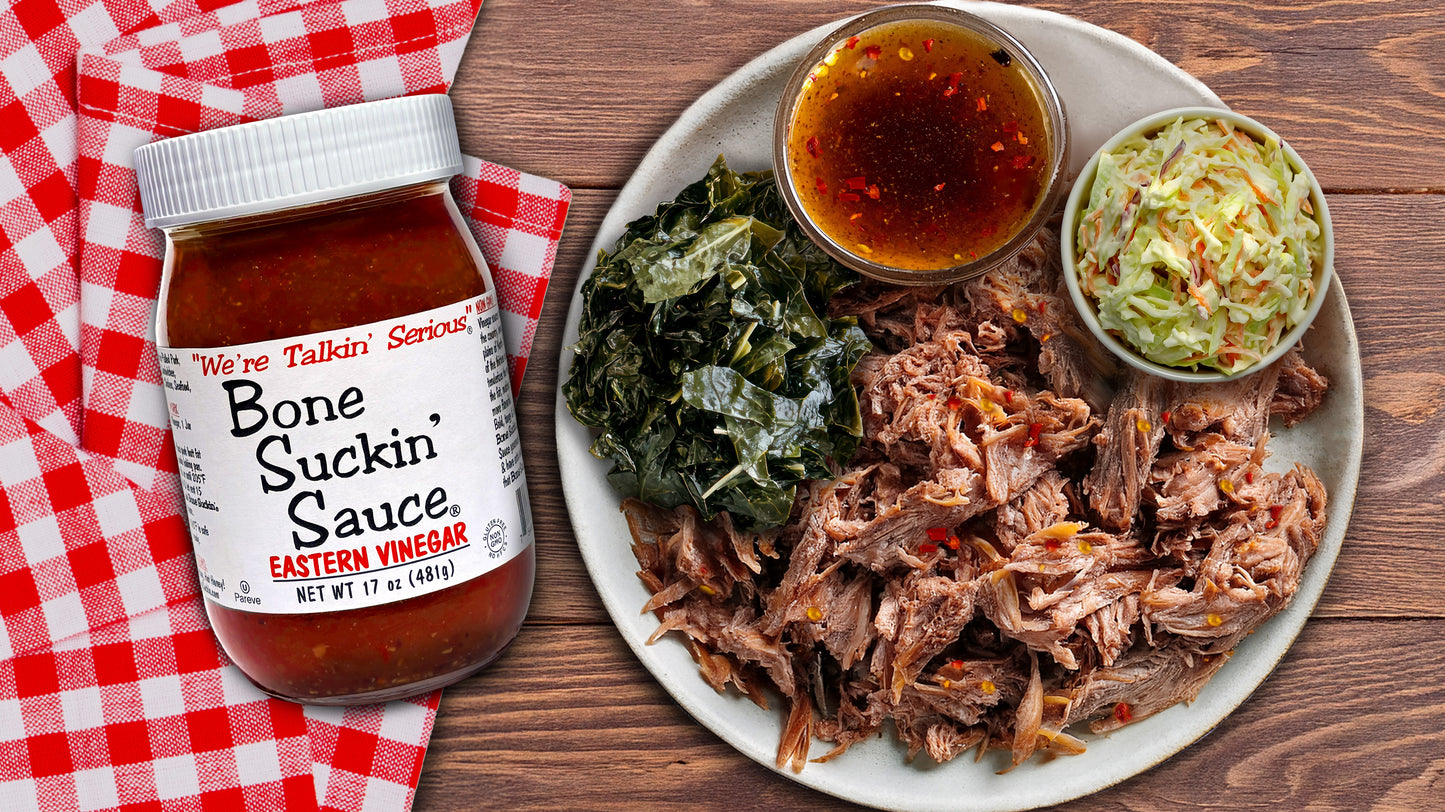 Plate of pulled pork with sides and a jar of Bone Suckin' Sauce Eastern Vinegar on a checkered tablecloth.