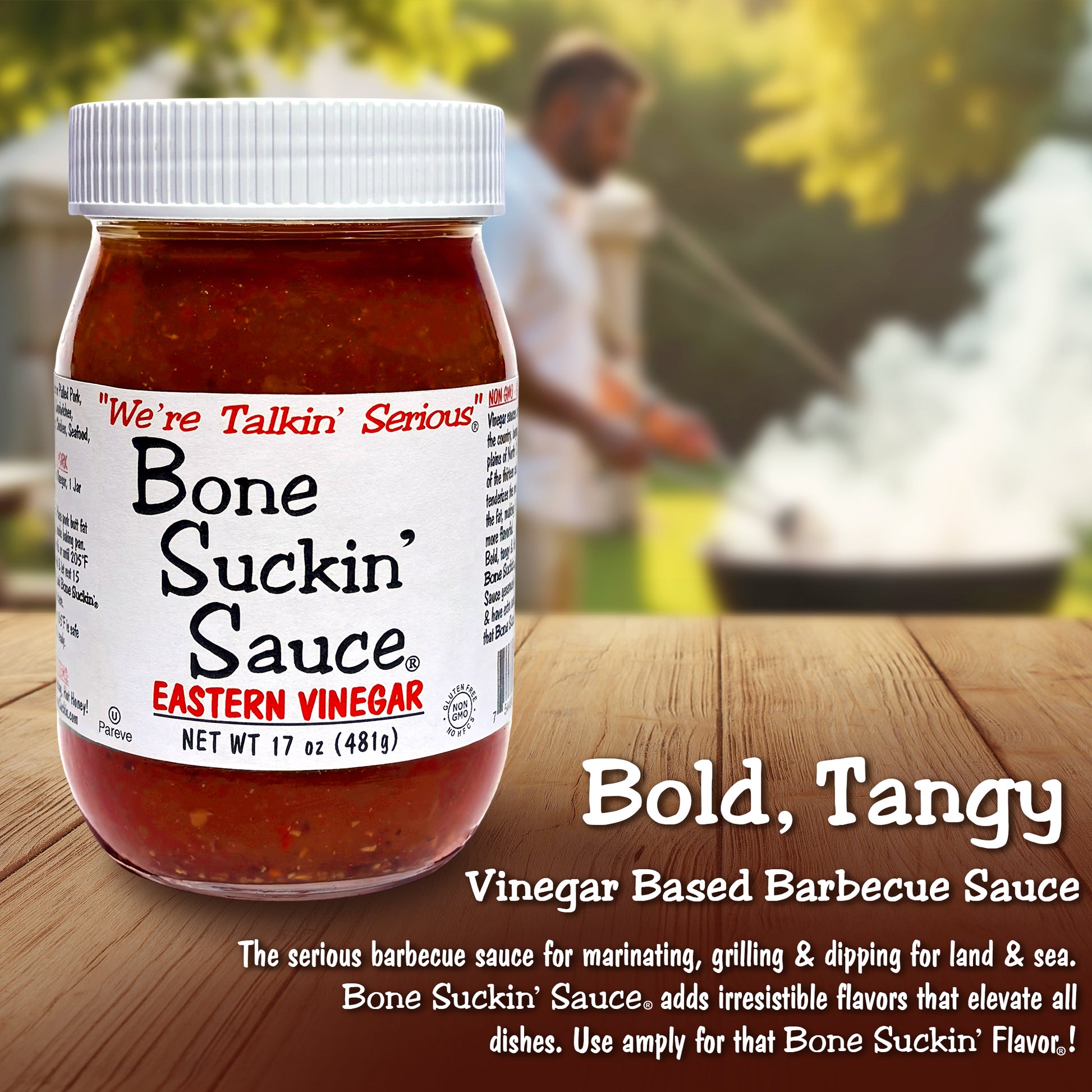Jar of Bone Suckin' Sauce on a wooden surface with a blurred background of a man grilling. - Bold, Tangy Vinegar Based Barbecue Sauce. The serious barbecue sauce for marinating, grilling, & dipping for land & sea. Bone Suckin' Sauce adds irresistible flavors that elevate all dishes. Use amply for that Bone Suckin' Flavor!